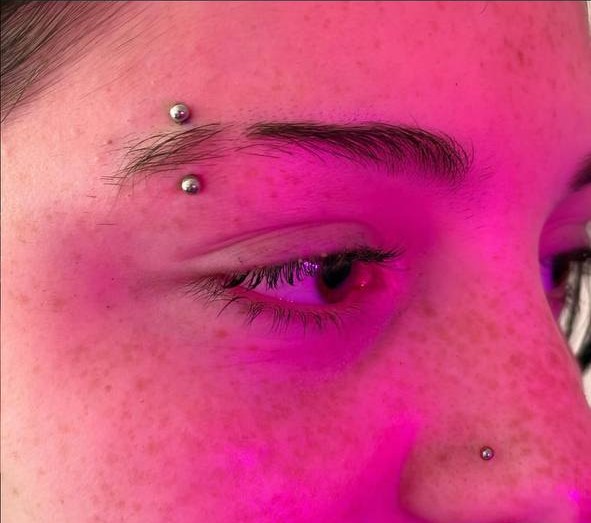 fresh nostril and traditional eyebrow piercings under pink uv light